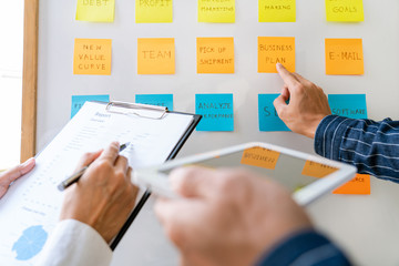 Business people arranging sticky notes commenting and brainstorming on work priorities colleague in...