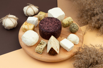Tasting set of homemade goat cheese on a round wooden dish on a background of earth color. Beige, brown, sand geometric background. Top view.