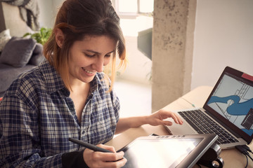 Young woman working from home due to the global pandemic. Illustrator working on the drawing tablet in her living room.