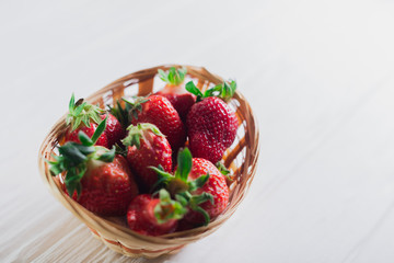 Juicy fresh strawberries in a basket on a white wooden background
