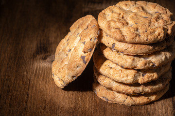 Close-up of chocolate chip cookies in stack, on wooden table, in dark light, horizontal, with copy space