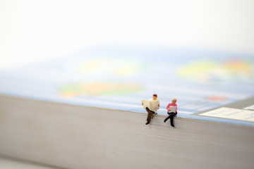 Miniature people sit on the book and reading a news paper with copy space for text.