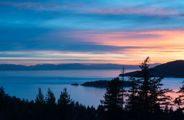 Panoramic view of Howe Sound and Vancouver Island at sunset. Foreground of Douglas Fir trees with a background of the Pacific Ocean.
