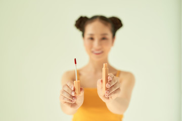 Portrait of cheerful beautiful Asian woman showing lipstick over light background.