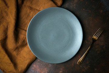 Empty plate on a dark background. Empty gray ceramic plate with a knife and fork for food and dinner on a dark beautiful background.