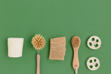 Layout of brushes made of bamboo and loofah on a green background. Zero waste concept with copy...