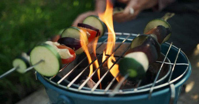 Young woman burning vegetable skewers on the barbecue