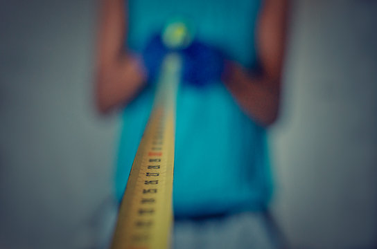 Conceptual photo of social distancing during Coronavirus crisis.  Selective focus on the yellow tape measure.  Blurry background of a black woman with gloves maintaining a safe distance.