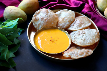 Indian Food - Aamras is a sweet dish made from the pulp of the Alphonso mango fruit. Served with hot puri/poori. Sweet Mango puree garnished with Kashmiri Saffron. with whole mangoes in background. 