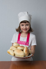 Little girl in a cook suit holds a plate with fresh pastries