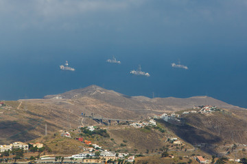 Top view of Gran Canaria mountains and sea on cloudy day. Nature landscape with small towns on valley and ships on background