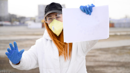 woman in protective mask holds sheet of clear white paper, looks at camera, shows stop sign with...