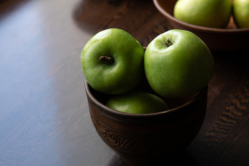 Green apples in a plate on a brown wooden table. Text space.
