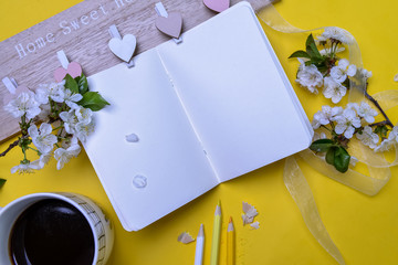 Spring backgound with white cherry blossom flowers, note book, cup and pencils for creative ideas. Hello spring concept composition over yellow background