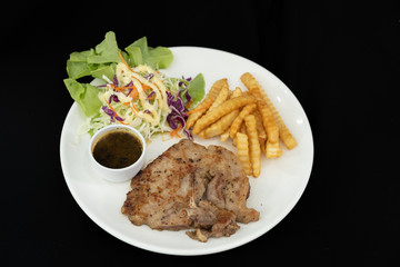 The plate of grilled pork steak with side dish french fries and salad. Black background.