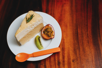 double fromage cheesecake served with sour fruit (passion fruit kiwi) in a white plate on a wooden table.Saw an orange spoon placed beside the plate