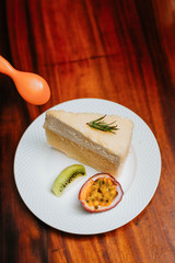 double fromage cheesecake served with sour fruit (passion fruit kiwi) in a white plate on a wooden table See an orange spoon from above