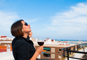 Fototapeta na wymiar Woman enjoy blue sky from her balcony with glass of red wine. Stay home. Lonely woman.