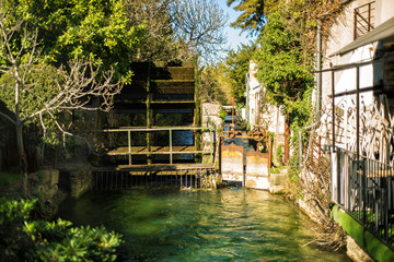 Wheel of a water mill in Medieval village L'Isle-sur-Sorgue, Vaucluse, Provence, France. Famous Sorgue river with green water. Provence travel tourism destination. Summer vacation in France.