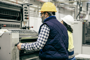 Two factory employees working with printing machine. Professional operators working at printing house. Print manufacturing concept