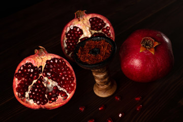A hookah smoking bowl filled with red pomegranate flavor tobacco lies next to a whole and cut...