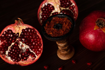 A hookah smoking bowl filled with red pomegranate flavor tobacco lies next to a whole and cut...