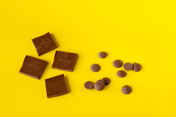 Milk chocolate bar and chocolate drops on a yellow background