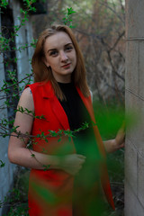 Fototapeta na wymiar a girl in a red suit and black blouse stands near a wall and a flowering tree