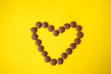 Drops of milk chocolate are placed in the heart on a yellow background
