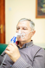 Fototapeta premium Senior man using medical equipment for inhalation with respiratory mask, nebulizer