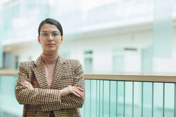 Portrait of young businesswoman in eyeglasses standing with arms crossed and looking at camera at office