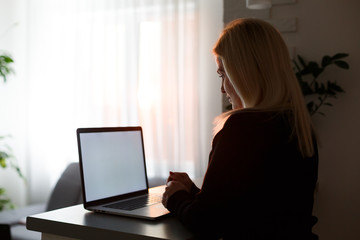 Unrecognizable woman working on her computer from her home office facing the spectacular metropolitan city at sunrise. Businesswoman doing research from a luxury hotel room