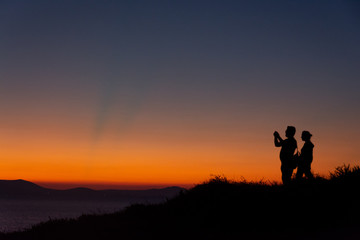 Silhouette of couple standing on mountain taking photo at sunset