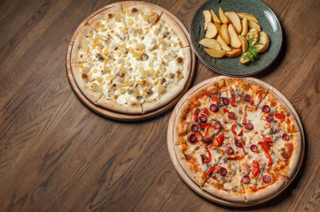 two pizzas and fried potatoes stand on a wooden table