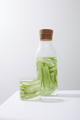 Bottle with cork and glass with drink made of sliced cucumbers isoated on grey