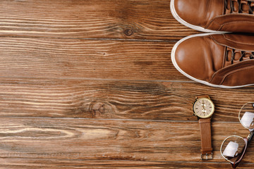 Top view of mens brown casual shoes, wristwatch and glasses on wooden background