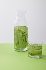 Bottle and glass with drink made of sliced cucumbers isolated on grey