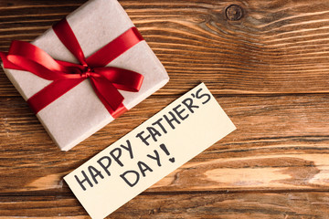 Top view of greeting card with lettering happy fathers day and pink gift box with red bow on wooden...