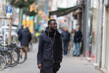 Young Black Man with Earphones Standing on Sidewalk with Head Turned