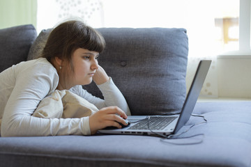 Naklejka premium Caucasian girl laying on the sofa with laptop,lockdown at home during coronavirus