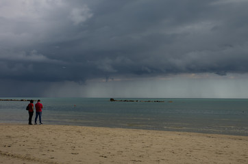 In the foreground, a man and a woman in the red shirt are watching the storm coming