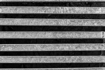 Black and white photo of an iron grate over a drainage channel on the road. Rusty texture on metal. Horizontal.