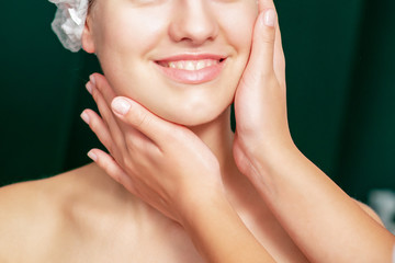 Hands of beautician touching face skin of smiling young woman.