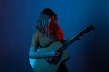Short hair girl is enjoying and playing her guitar in blue and red light.