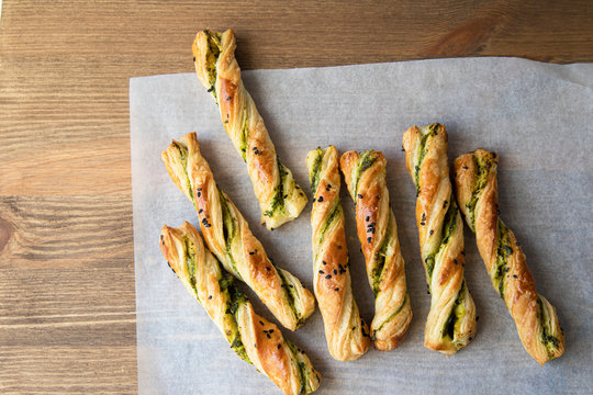 salty sticks of puff pastry sprinkled with cumin and greenery on a wooden background