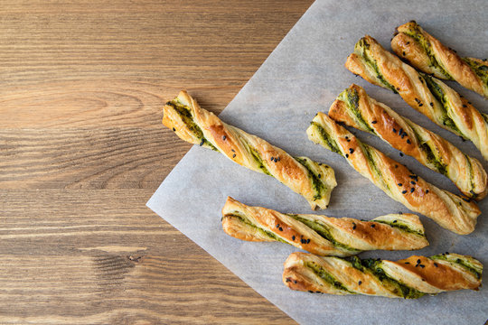 salty sticks of puff pastry sprinkled with cumin and greenery on a wooden background