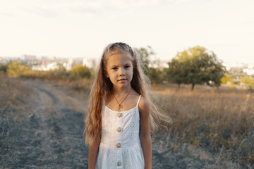 Lovely carefree little girl wearing white clothes enjoy the day and sunshine rays while playing in the nature