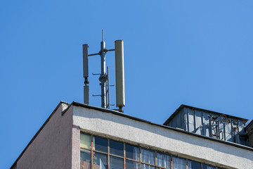 Cellular communication antenna on a flat roof of a multi-storey apartment building against blue sky on a sunny day.