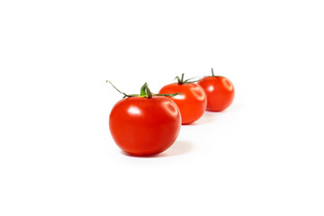 Three red tomatoes are standing one after another. Bright red color. Isolated objects. The background is blurry. Green stems. Glare about two light sources.