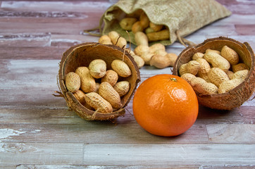 Peanuts lies in a coconut shell on a wooden table with orange tangerine fruit, healthy food.